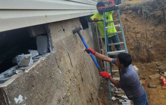 Foundation wall repair and stabilization with workers reinforcing damaged concrete block wall